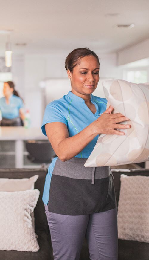 house maid fluffing a pillow from a couch 