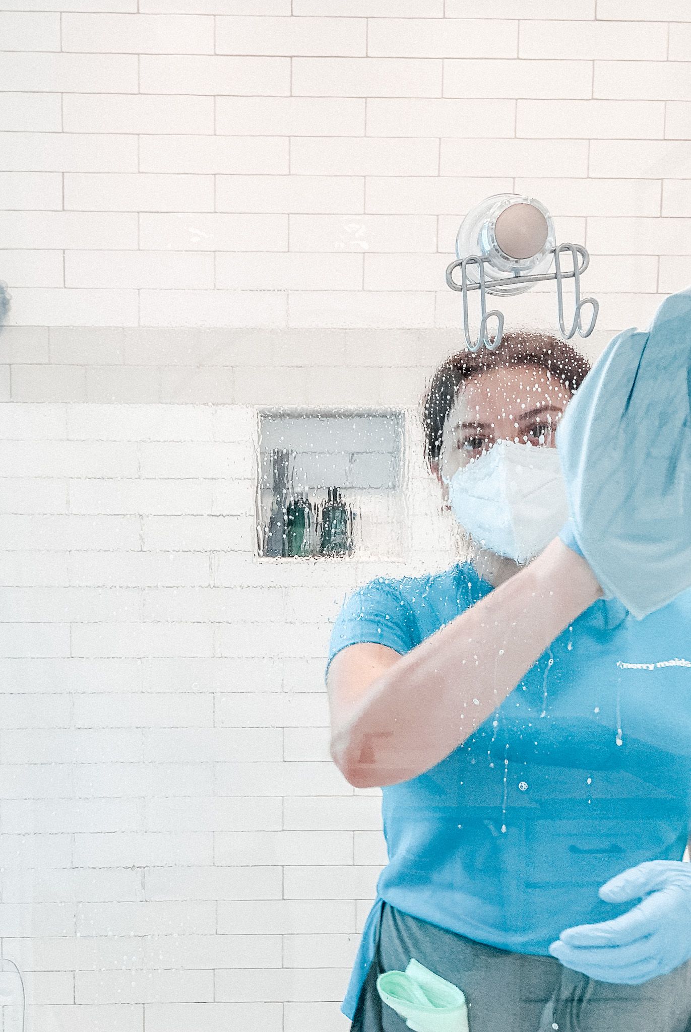 Merry Maids team member wearing PPE and disinfecting glass inside a bathroom