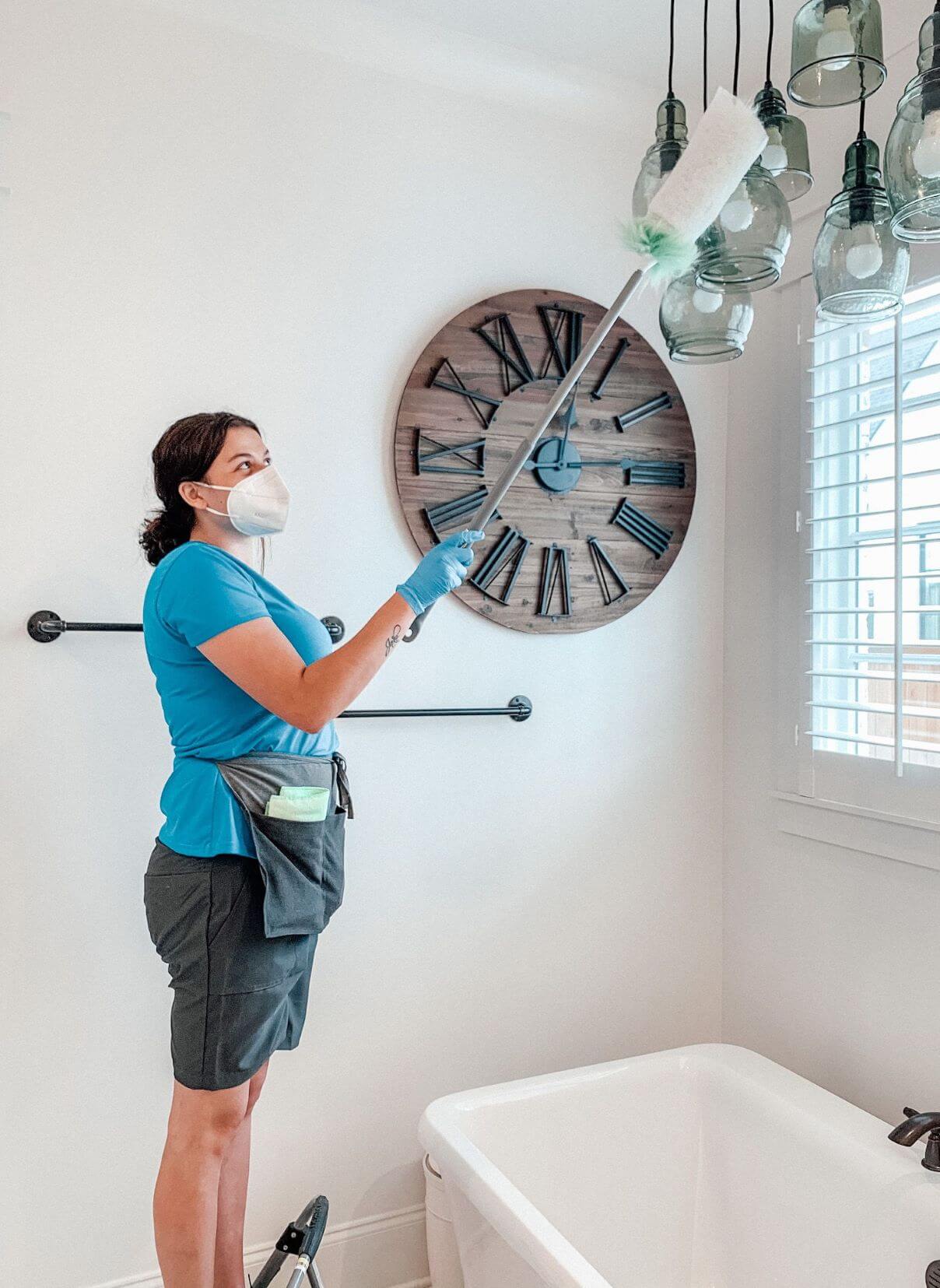 Merry Maids professional deep cleaning a bathroom by dusting the lights above the bath tub